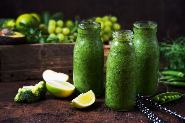 Tres botellas del licuado verde más saludable de vegetales y frutas y alrededor de los vegetales y frutas verdes. Foto horizontal