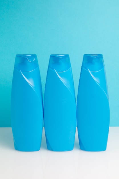 Tres botellas de plástico con champú sobre un fondo azul.