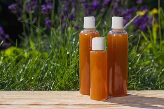 Tres botellas de plástico de diferentes tamaños con gel se colocan sobre la madera. Hay hierba verde y arbustos de lavanda en el fondo.