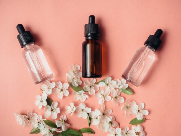 Tres botellas de vidrio con aceite, perfume en una superficie rosa con cereza en flor. Lay Flat, minimalismo.