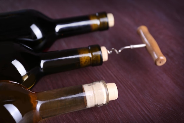 Tres botellas de vino y sacacorchos sobre fondo de madera púrpura
