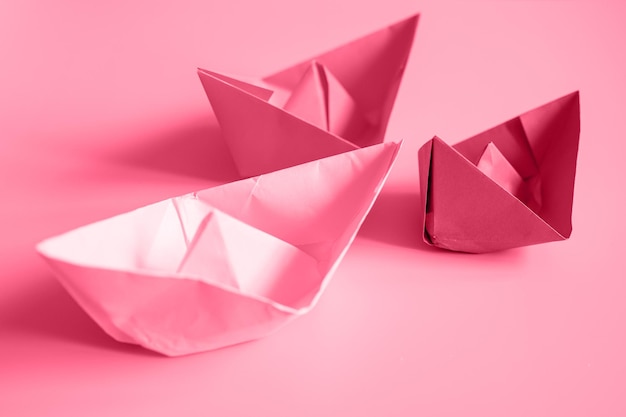 Tres botes de origami de papel de colores brillantes en colores púrpura sobre un fondo rosa tonificado en el color de tendencia magenta viva del año 2023