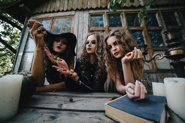 Tres brujas antiguas realizan un ritual mágico, arrojando dulces a una mesa en la víspera de Halloween