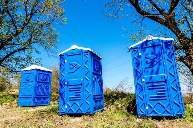 Três cabines azuis dos toaletes químicos em um parque no dia de verão ensolarado.