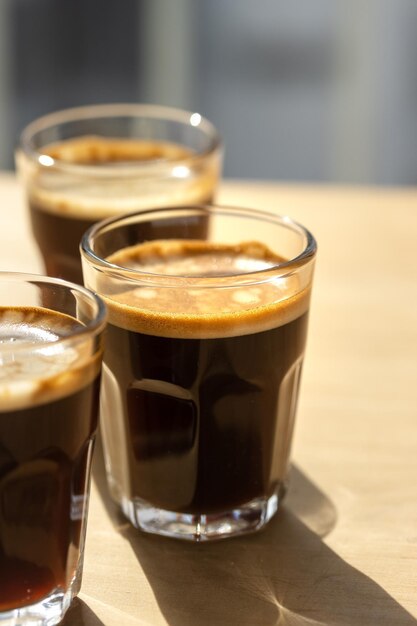 Tres cafés espresso en vasos de vidrio sobre una mesa de madera Copiar composición espacial con sombras