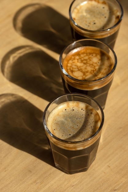 Tres cafés espresso en vasos de vidrio sobre una mesa de madera Copiar composición espacial con sombras