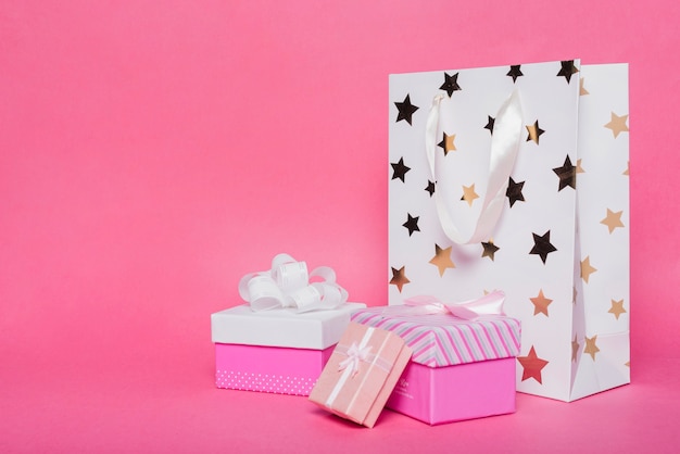 Foto tres cajas de regalo y bolsa de papel de compras en el contexto rosado