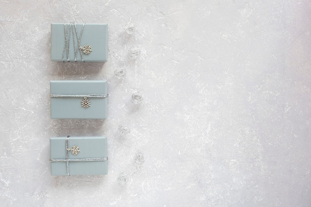 Tres cajas de regalo grises decoradas con cinta plateada y colgante de copo de nieve, sobre fondo gris, vista superior, espacio de copia
