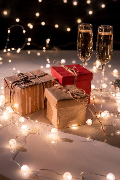 Tres cajas de regalo llenas, dos copas de champán en la mesa decorada con guirnaldas iluminadas para la fiesta de año nuevo