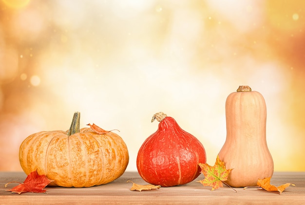 Tres calabazas en una fila y hojas de otoño sobre una mesa de madera