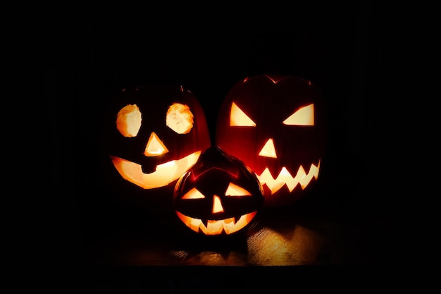 Tres calabazas Jacko'lantern cerca de la chimenea en llamas en la oscuridad