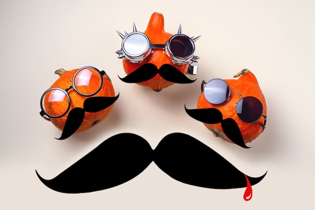 Tres calabazas mecedoras naranjas con gafas y bigote sobre un fondo claro. Concepto de Halloween.