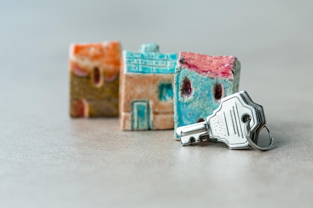 Tres casas de cerámica de juguete que simbolizan bienes raíces con llaves de metal al lado