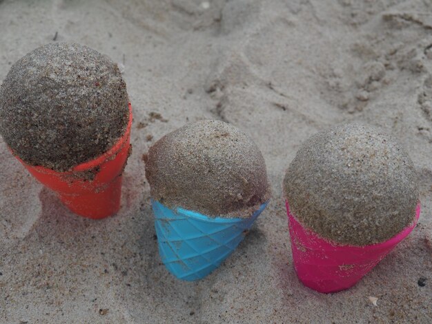 Três casquinhas de sorvete estão na areia.