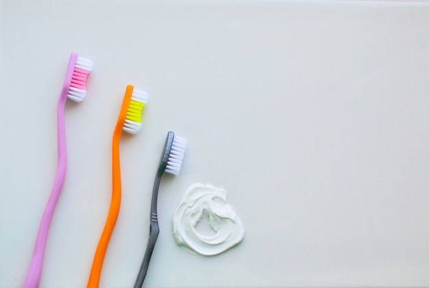 Foto tres cepillos de dientes sobre un fondo blanco y pasta de dientes blanca