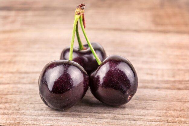 Três cerejas maduras em fundo de madeira