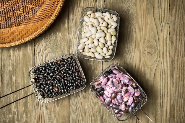 Tres cestas de metal con frijoles coloridos sobre una mesa de madera áspera