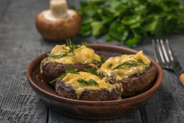 Tres champiñones al horno con hierbas sobre una mesa de madera. Un plato de setas al horno con queso.