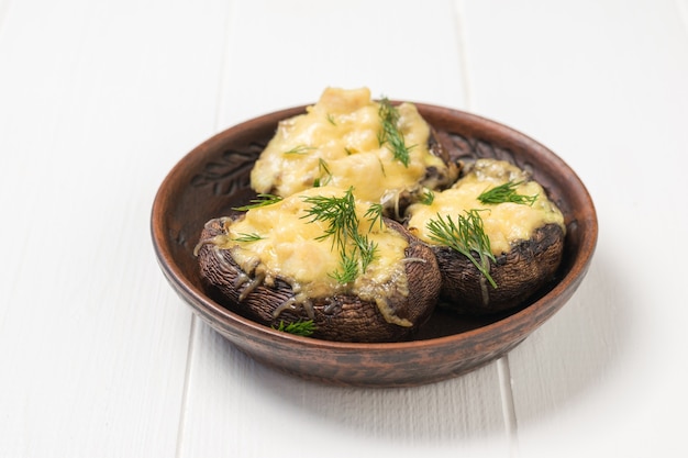 Tres champiñones al horno con queso y pechuga de pollo sobre una mesa blanca. Un plato de setas al horno con queso.