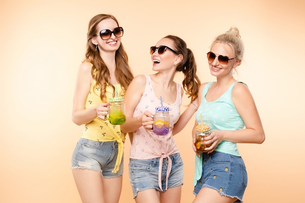 Foto tres chicas deportivas bebiendo jugo fresco y posando