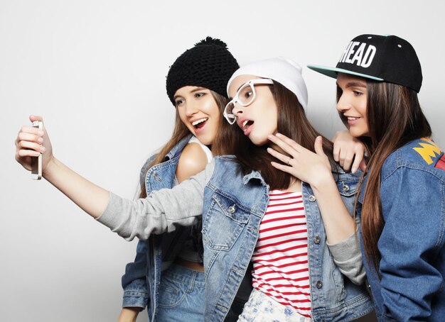 Tres chicas hipster adolescentes felices con smartphone tomando selfie