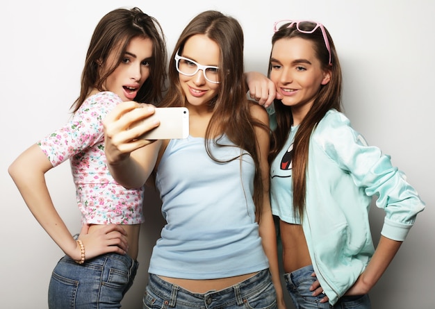 Tres chicas hipster adolescentes felices con smartphone tomando selfie