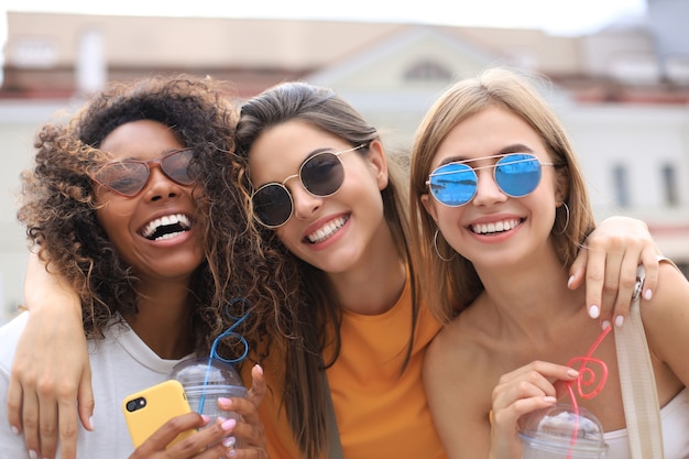 Tres chicas hipster cool de moda, amigos beben cócteles en el fondo de la ciudad urbana.