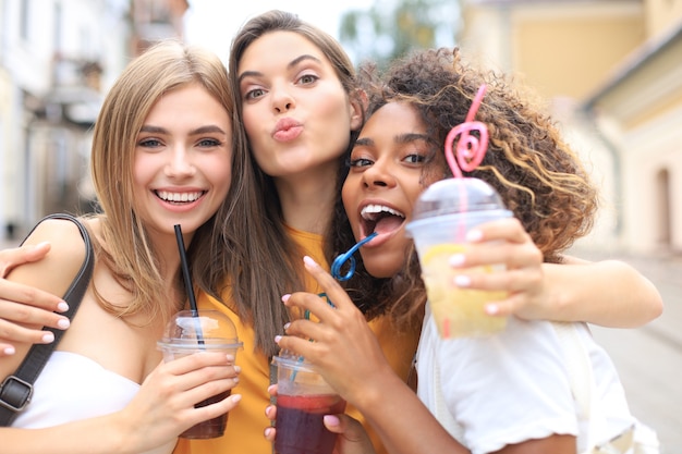 Tres chicas hipster cool de moda, amigos beben cócteles en el fondo de la ciudad urbana.