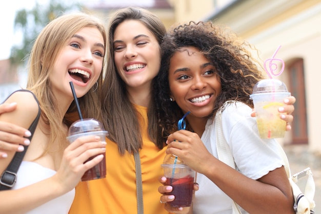 Tres chicas de moda hipster cool, amigos beben cócteles en el fondo de la ciudad urbana.