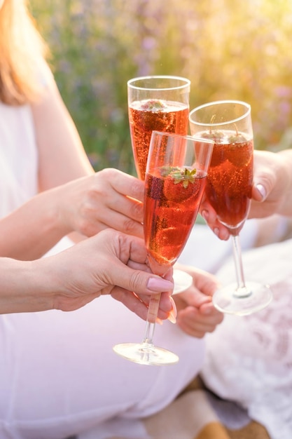 Tres chicas tintinean copas con vino espumoso y fresas en un picnic