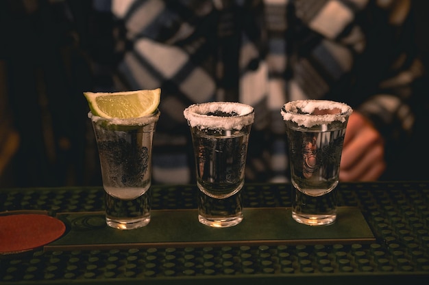 Foto tres chupitos de tequila bordeados con sal servidos con lima en la barra del bar