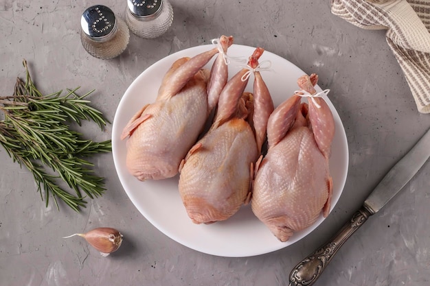 Tres codornices orgánicos frescos en un plato blanco sobre un fondo gris Vista superior del primer