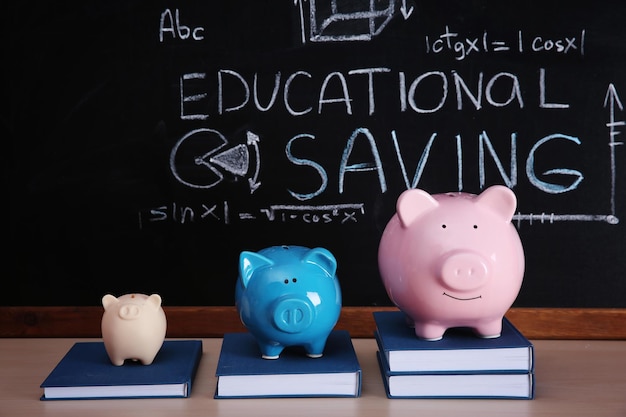 Três cofrinhos com livros sobre fundo de quadro-negro Conceito de poupança educacional