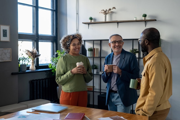 Três colegas de sucesso em roupas casuais inteligentes tomando bebidas no intervalo