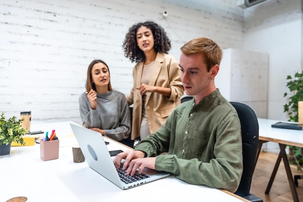 Três colegas discutindo e usando laptop em um espaço de coworking