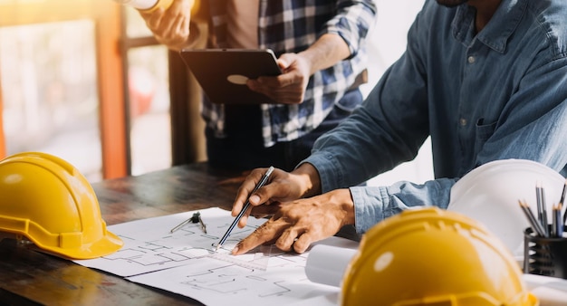 Três colegas discutindo o trabalho de dados e o laptop tablet com um projeto arquitetônico no canteiro de obras na mesa do escritório