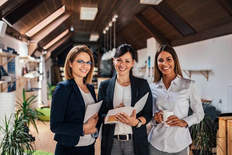 Três colegas fêmeas em uma reunião do trabalho que sorriem à câmera.