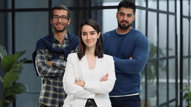 Tres colegas de pie en el vestíbulo de una oficina moderna con los brazos cruzados