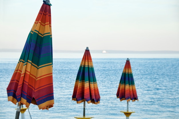 Tres coloridas sombrillas frente al mar.