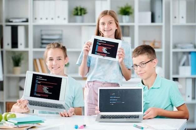 Tres compañeros de clase felices y exitosos que muestran sus presentaciones en pantallas de dispositivos móviles después de terminarlas