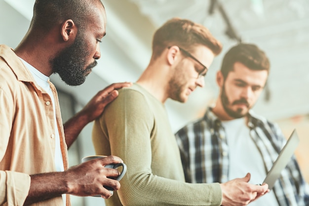 Tres compañeros de trabajo masculinos se concentran en la pantalla del portátil