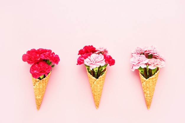 Tres conos de helado de gofre con flores de clavel rosa sobre fondo rosa espacio de copia de vista superior