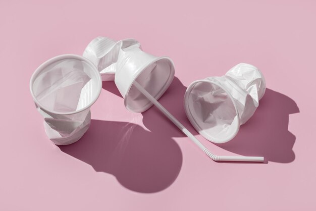 Foto três copos de plástico brancos com canudos em um fundo rosa. longas sombras, tiro de estúdio.