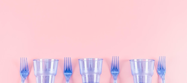 Três copos de plástico transparentes azuis e quatro garfos em um fundo rosa