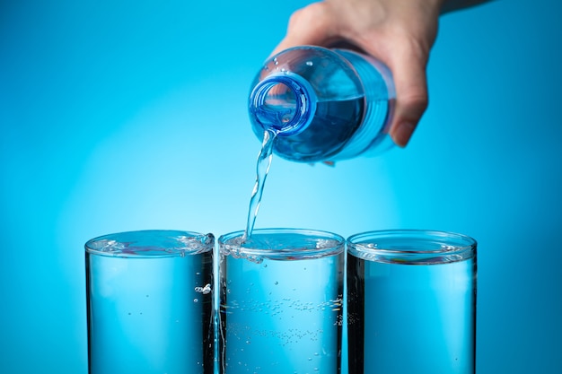 Foto três copos transparentes são enchidos com água de uma garrafa em um fundo azul.