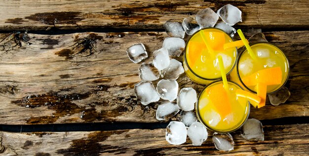 Três coquetéis de laranjas frescas com gelo e palha no fundo de madeira