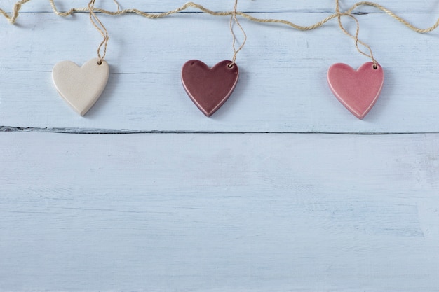 três corações de cerâmica são pendurados em uma corda em um fundo branco de madeira