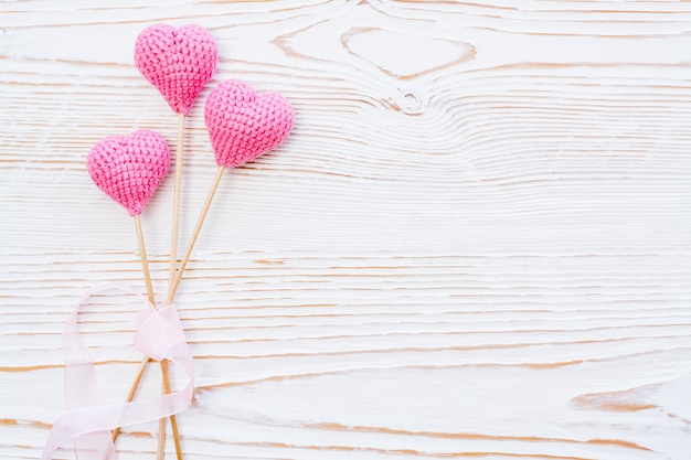 Três corações de malha-de-rosa com fita rosa em um fundo branco de madeira