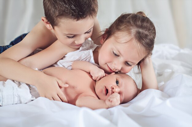 Três crianças alegres em casa, bebê recém-nascido com irmão e irmã, família feliz, conceito de amor e amizade