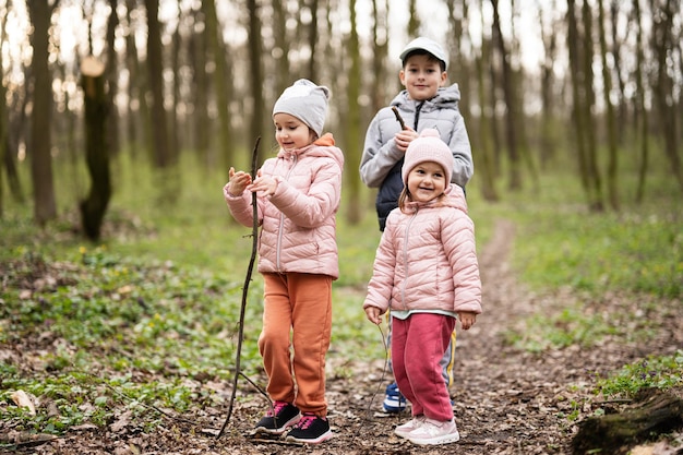 Três crianças caminhando e descobrindo a floresta da primavera Infância feliz